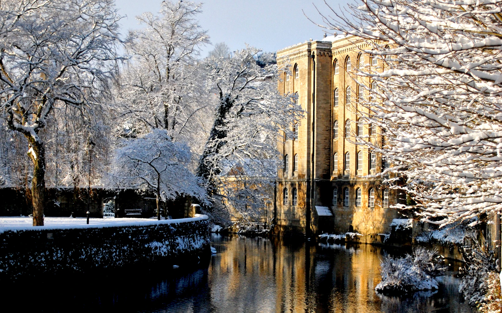 Snow-covered trees and a stone riverside building reflected in the water in Bradford-on-Avon, Wiltshire